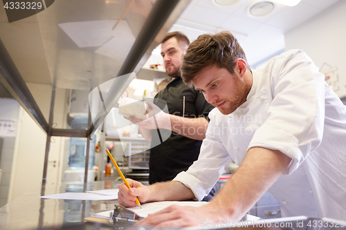 Image of chef and cook with lists or bills at kitchen