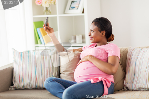 Image of pregnant woman taking smartphone selfie at home
