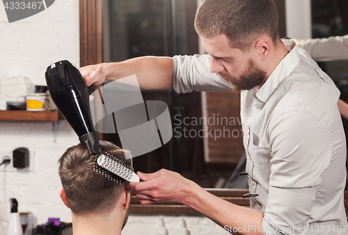 Image of Young handsome barber making haircut of attractive man in barbershop