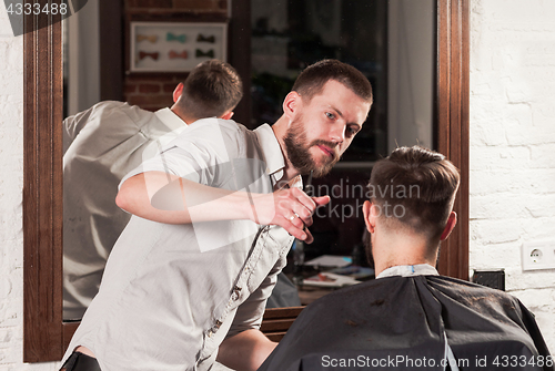 Image of Young handsome barber making haircut of attractive man in barbershop