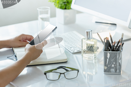 Image of Close-up of female hands using smart phone while working on computer at modern office interior