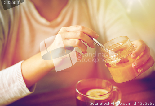 Image of close up of woman adding honey to tea with lemon