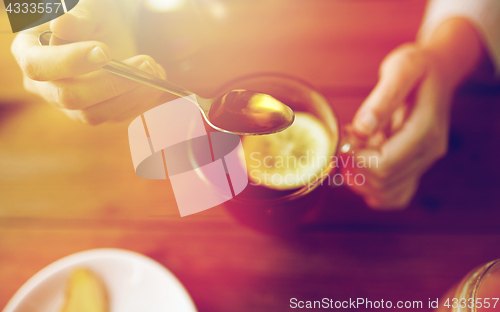 Image of close up of woman adding honey to tea with lemon