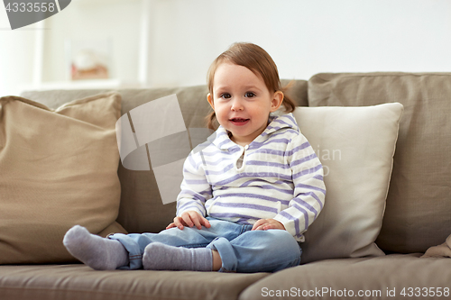 Image of happy smiling baby girl sitting on sofa at home