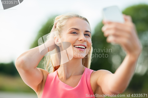 Image of happy woman taking selfie with smartphone outdoors