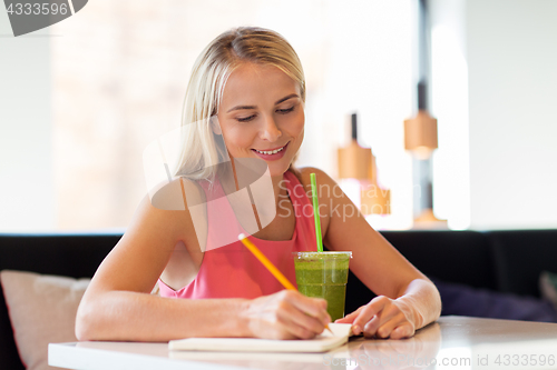 Image of woman with drink writing to notebook at restaurant