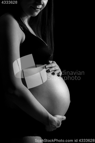 Image of Pregnant woman caressing her belly isolated on black monochrome background.