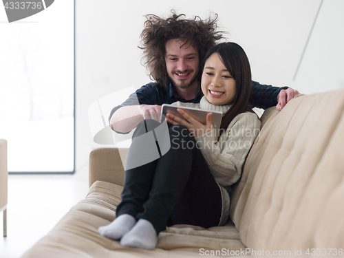 Image of multiethnic couple at home using tablet computers