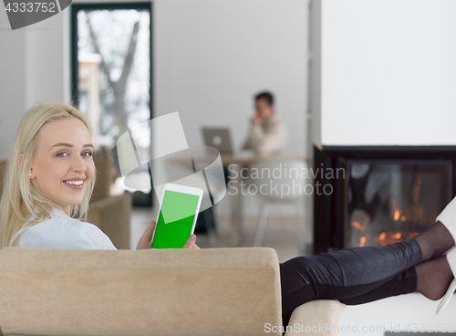 Image of young woman using tablet computer in front of fireplace