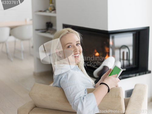 Image of young woman using tablet computer in front of fireplace