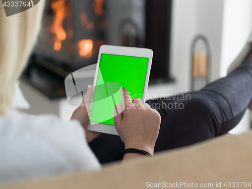 Image of young woman using tablet computer in front of fireplace