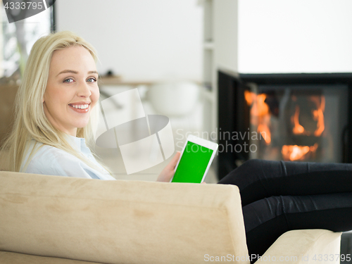 Image of young woman using tablet computer in front of fireplace