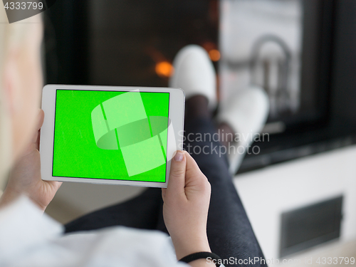 Image of young woman using tablet computer in front of fireplace