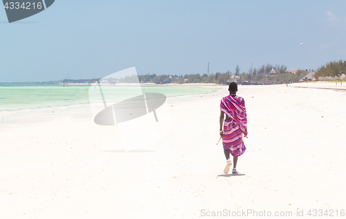 Image of Maasai warrior walking on picture perfect tropical sandy beach. Paje, Zanzibar, Tanzania.