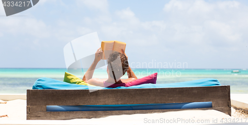 Image of Relaxed man reading book in luxury lounger enjoying summer vacations on beautiful beach.