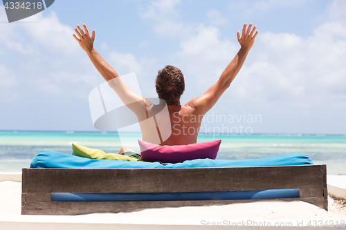 Image of Relaxed man in luxury lounger, arms rised, enjoying summer vacations on beautiful beach.