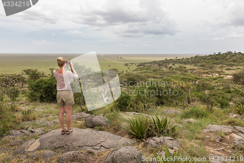 Image of Female tourist looking through binoculars on African safari in Serengeti national park. Tanzania, Afrika.