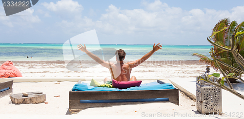 Image of Relaxed man in luxury lounger, arms rised, enjoying summer vacations on beautiful beach.