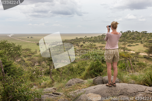 Image of Female tourist looking through binoculars on African safari in Serengeti national park. Tanzania, Afrika.