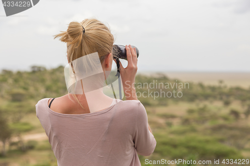 Image of Female tourist looking through binoculars on African safari in Serengeti national park. Tanzania, Afrika.