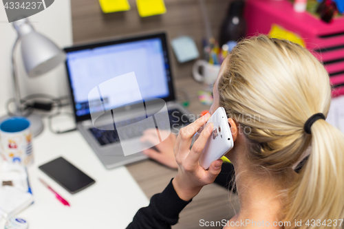 Image of Female entrepreneur talking on mobile phone in colorful modern creative working environment.