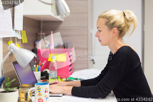 Image of Female entrepreneur working on laptop in colorful modern creative working environment.