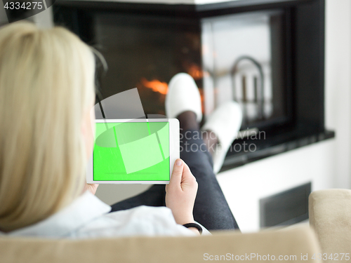 Image of young woman using tablet computer in front of fireplace