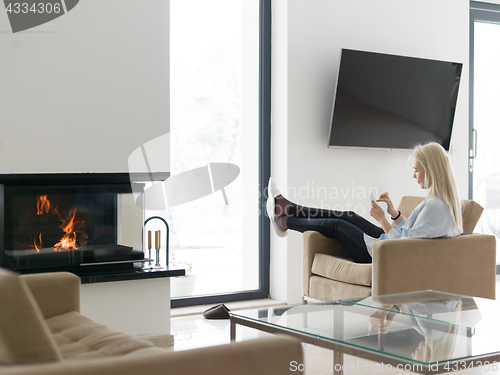 Image of young woman using tablet computer in front of fireplace