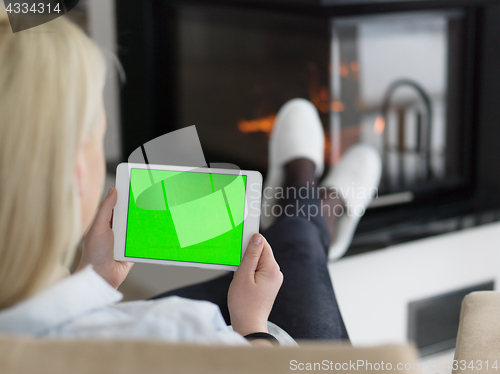 Image of young woman using tablet computer in front of fireplace