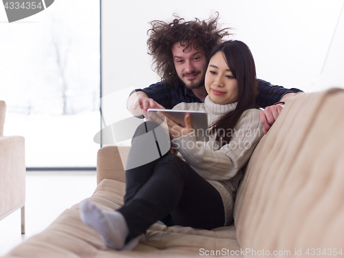 Image of multiethnic couple at home using tablet computers