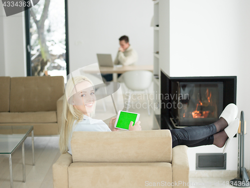 Image of young woman using tablet computer in front of fireplace