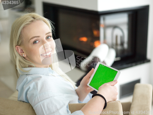 Image of young woman using tablet computer in front of fireplace