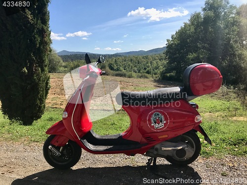 Image of Close up red color vintage scooter for rent by Siena Vespa in Tuscan landscape