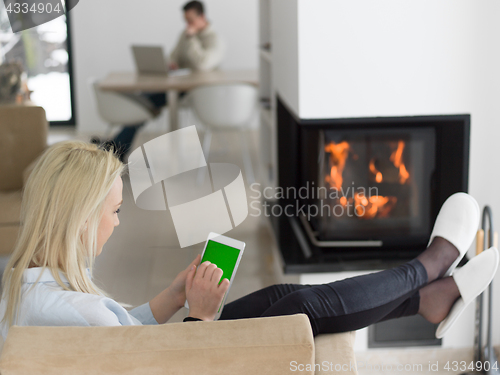 Image of young woman using tablet computer in front of fireplace