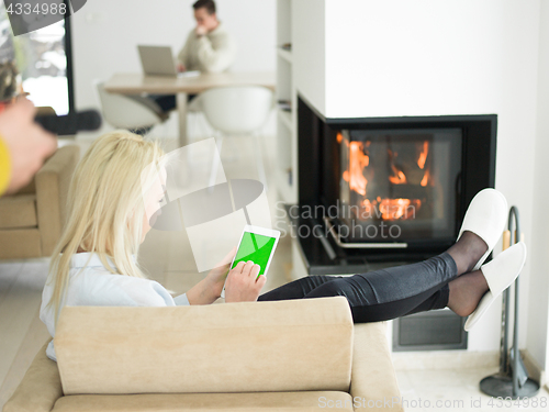 Image of young woman using tablet computer in front of fireplace