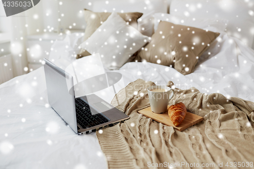 Image of laptop, coffee and croissant on bed at cozy home