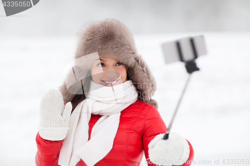 Image of happy woman with selfie stick outdoors in winter