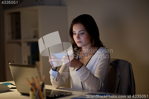 Image of businesswoman with smartphone and laptop at office