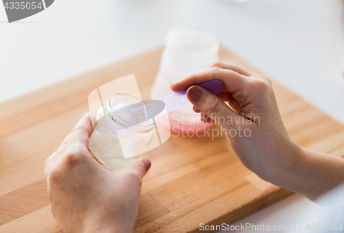 Image of hands with jar and scoop making formula milk