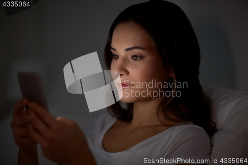 Image of happy young woman with smartphone in bed at night