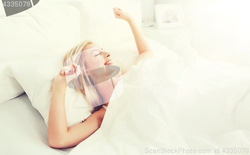 Image of young woman stretching in bed at home bedroom