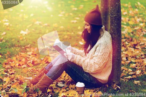 Image of woman with book drinking coffee in autumn park