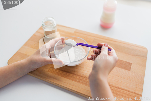 Image of hands with spoon and jar making baby cereal