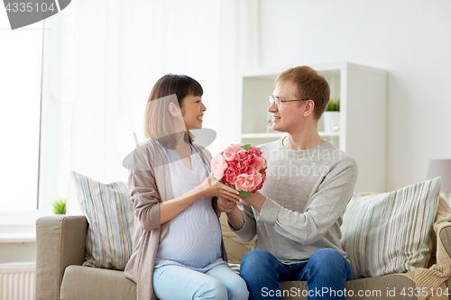 Image of happy husband giving flowers to his pregnant wife