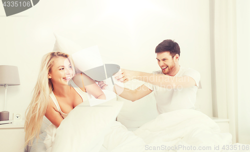 Image of happy couple having pillow fight in bed at home