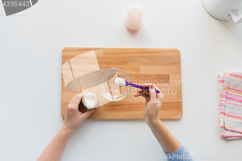 Image of hands with spoon and jar making baby cereal