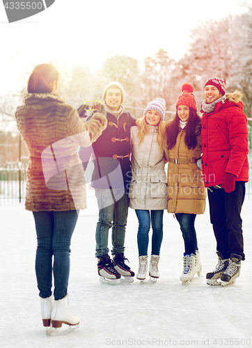 Image of happy friends with smartphone on ice skating rink