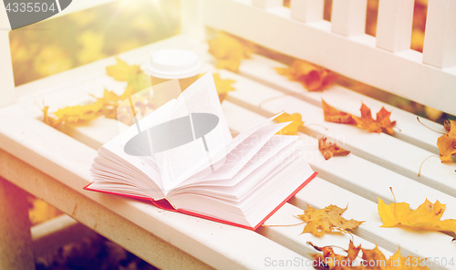 Image of open book and coffee cup on bench in autumn park