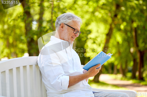 Image of happy senior man reading book at summer park