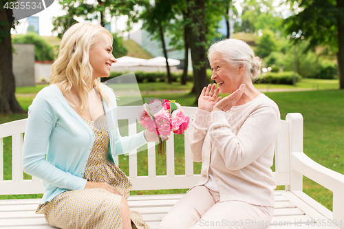 Image of daughter giving flowers to senior mother at park